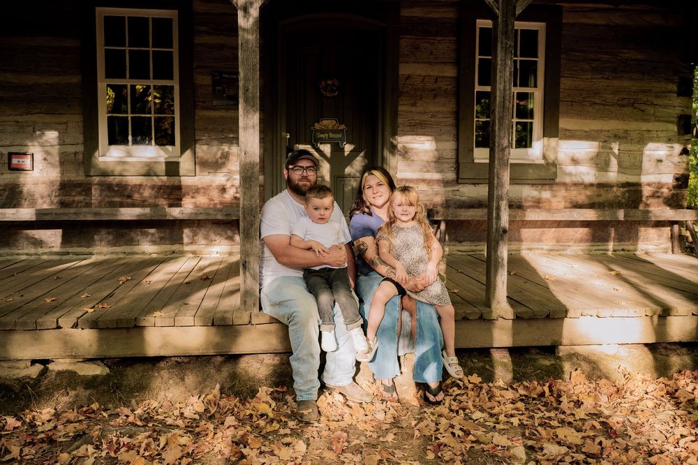 Rustic wooden cabin backdrop with autumn leaves scattered on the ground during a family photo session.
