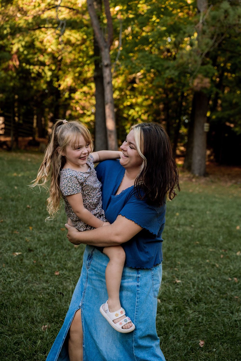 A playful outdoor photoshoot in a sunlit park with autumn trees in the background.