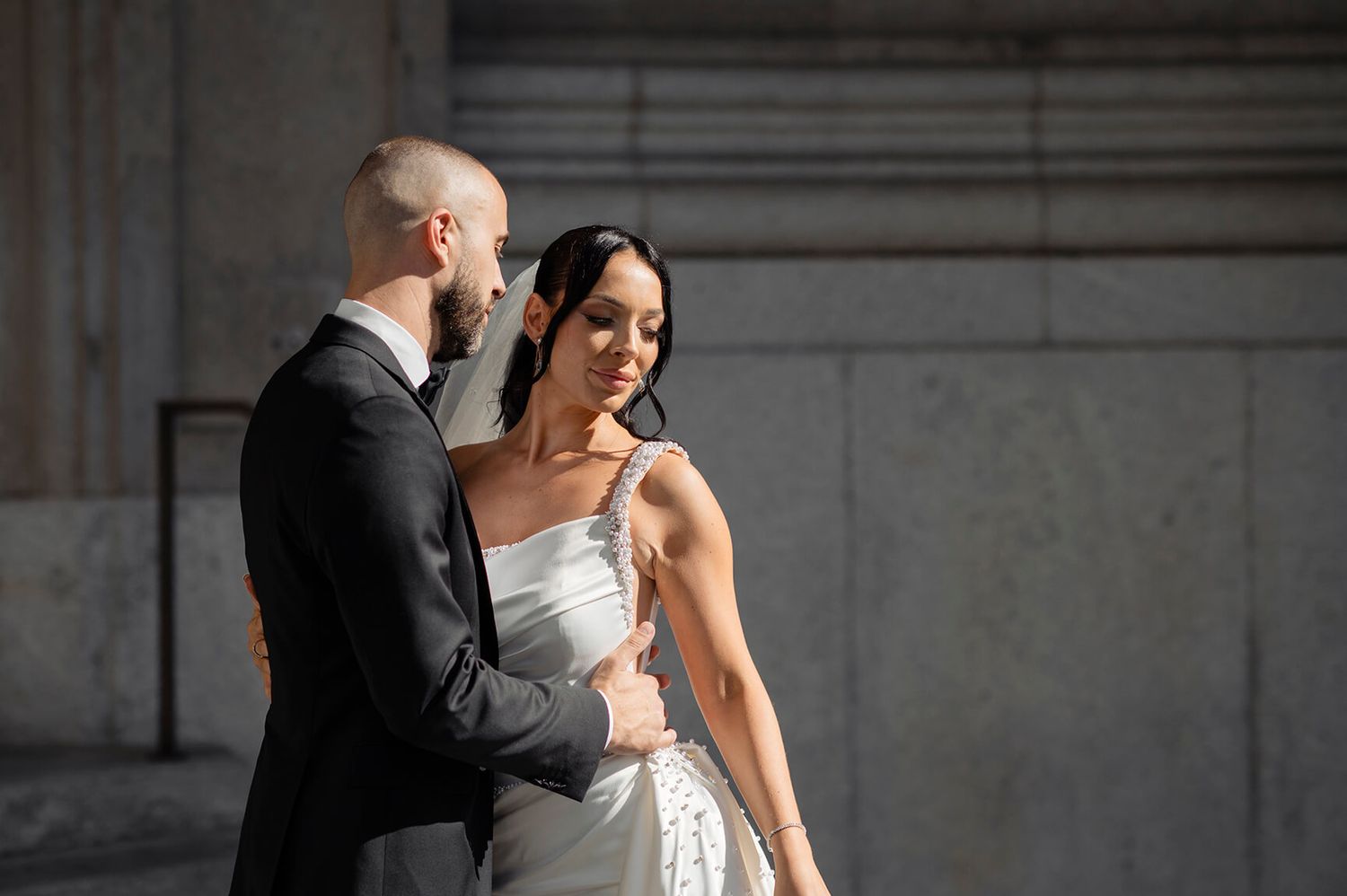 Elegant wedding couple shares an intimate moment in front of a classic stone building.