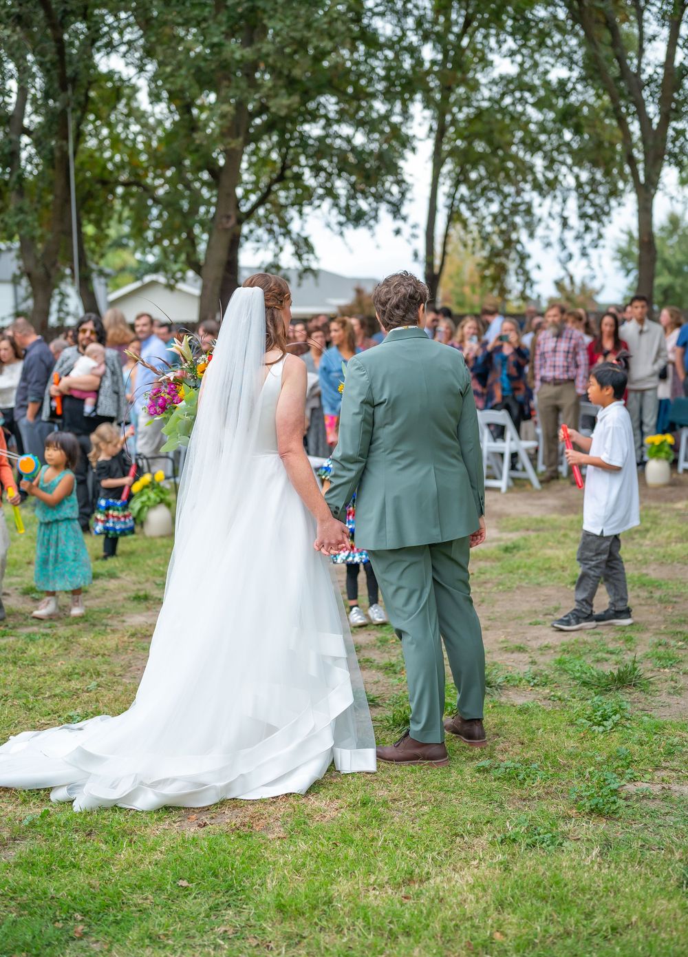 A wedding couple dances together outdoors surrounded by guests on a grassy area during their special day celebration.