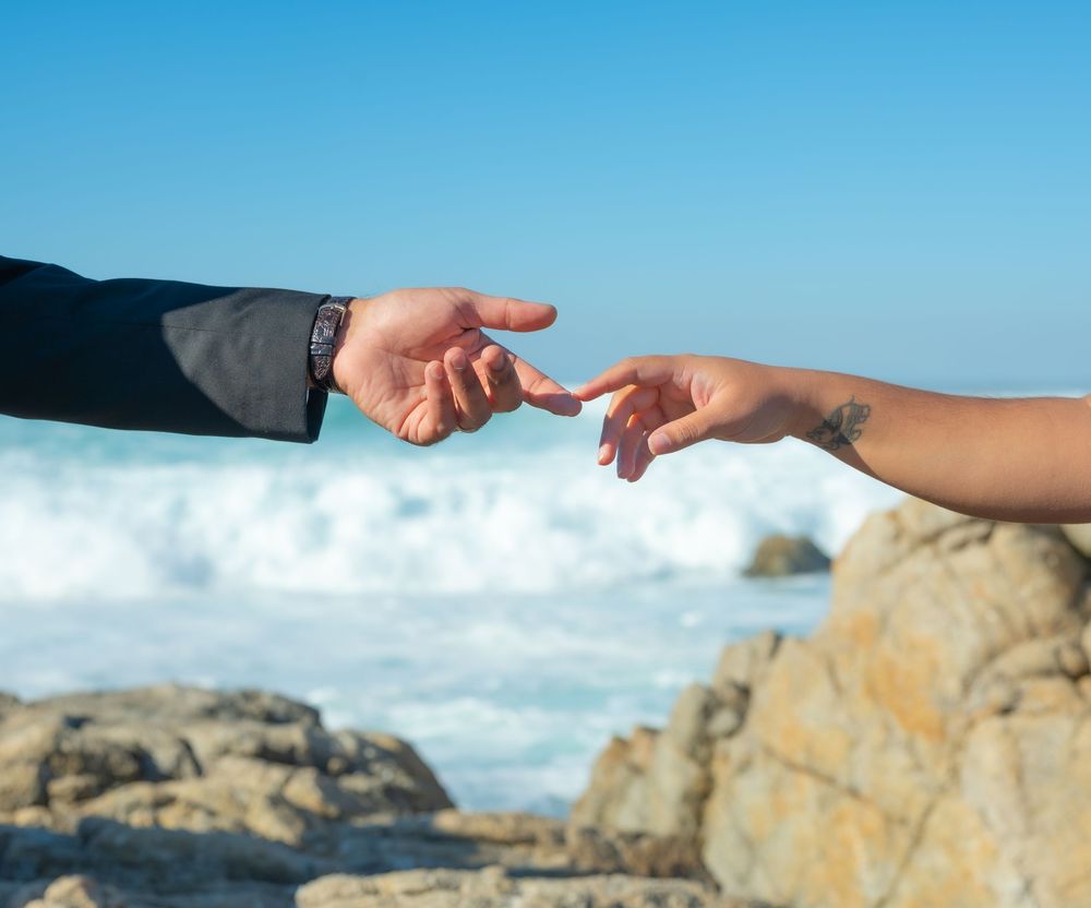 A series of hands reaching out to connect in sequence against a bright blue sky and rocky coastal background.