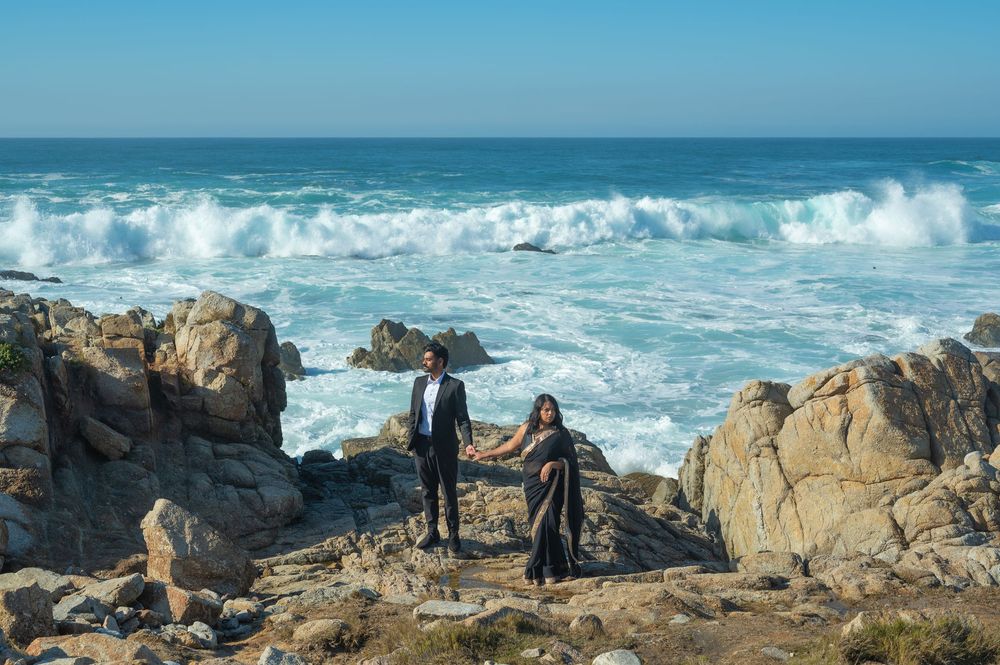 Dramatic coastal landscape with crashing waves against rugged rock formations along a scenic shoreline under blue skies.