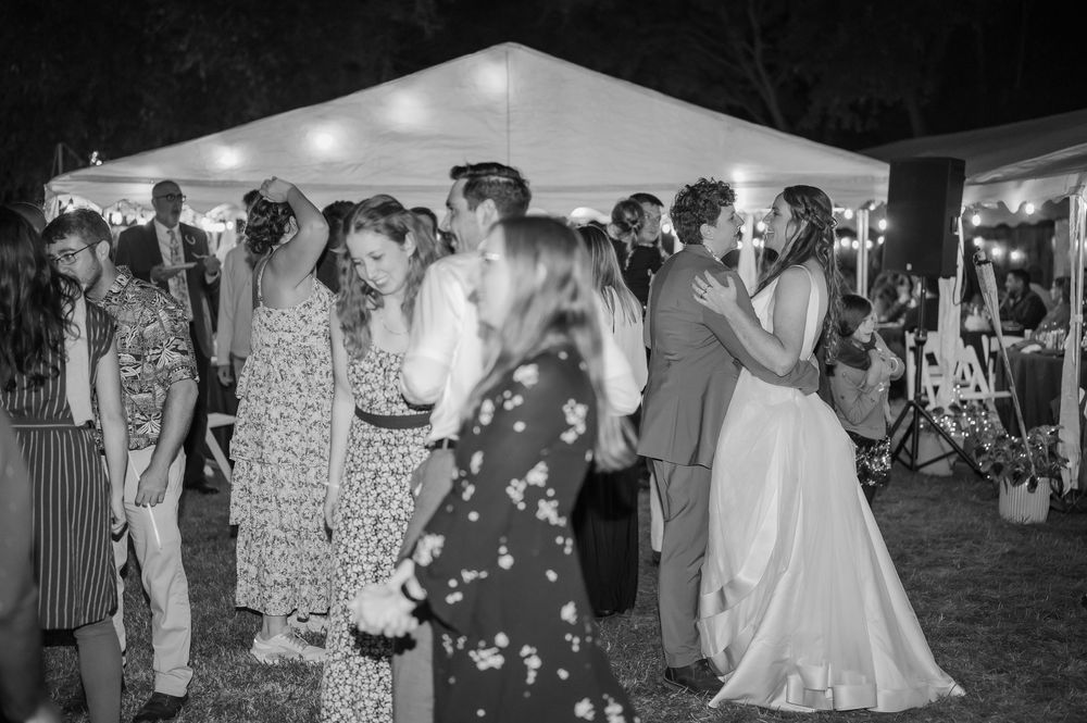 Couples dancing under string lights at an outdoor wedding reception beneath a white tent at night.