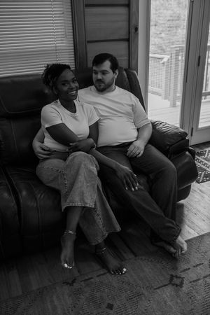 A couple sits together intimately on a couch in a black and white series of candid photographs.