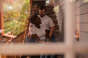 A couple sits together on wooden stairs in a warmly lit interior space with a dreamy, romantic atmosphere.