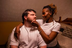 A playful couple in white t-shirts share a lighthearted moment together indoors.