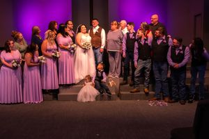 Wedding party gathered on stage with purple lighting and bridesmaids in pink dresses.