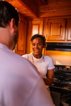 A couple shares a joyful conversation in a warm-lit kitchen with wooden cabinets.
