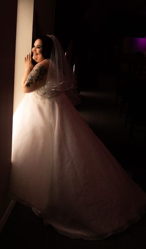 A bride in a flowing white wedding gown laughs joyfully while standing in dramatic side lighting against a dark background.