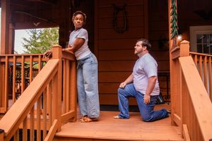 People sitting on a rustic wooden porch with brown stained railings and posts during a gathering.