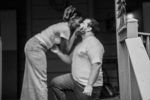 A tender moment captured in black and white as two people share an affectionate kiss on a porch.