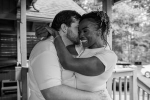 An intimate black and white portrait of a couple embracing on a porch.