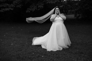 A bride in a flowing white dress twirls and dances outdoors in a black and white photograph.