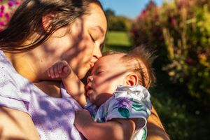 A tender moment between parent and child in a sunlit garden with pink flowers in the background.