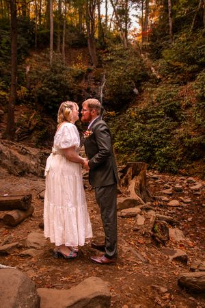 A couple shares a romantic moment on rocky terrain surrounded by autumn foliage in a forest setting at sunset.