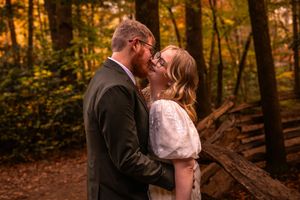 A romantic wedding couple embraces in a sunlit autumn forest with golden leaves and rustic wooden elements.