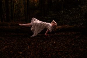 A ghostly figure in white fabric lies on dark forest ground creating an eerie and haunting scene in nature.