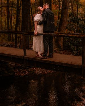 A couple embraces on a wooden bridge surrounded by autumn trees at sunset creating a romantic forest atmosphere.