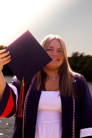 Graduate poses with graduation cap in a series of playful photos wearing white top and dark gown at sunset.