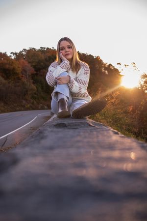 A person sits on a concrete road at sunset wearing white sneakers and jeans in a warm golden light.