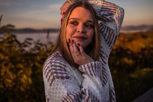 A person in a cozy white sweater poses against a warm sunset backdrop in nature during golden hour.