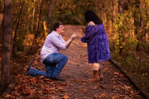 A couple poses together on a wooded path during a romantic autumn engagement photo session.