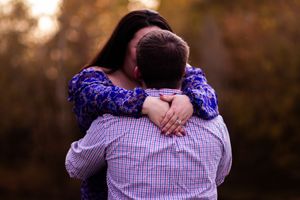 A couple embraces in a warm sunset glow wearing purple and plaid clothing in an outdoor setting.