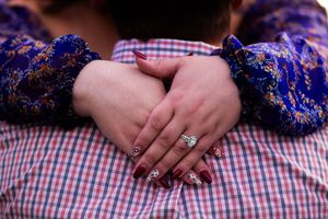 Close-up of hands wearing engagement ring with blue and pink plaid fabric in background.