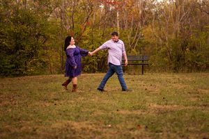 Two people dance together playfully in a grassy field during autumn with trees in the background.
