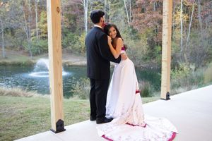 A romantic couple shares a tender moment on a covered porch overlooking a pond with a fountain in autumn.