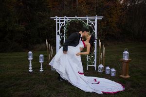 A romantic moment under a white arch decorated with lanterns during an outdoor autumn wedding ceremony.