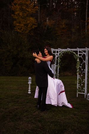 A couple dances together in front of a white arch decorated with lanterns during an outdoor autumn wedding.