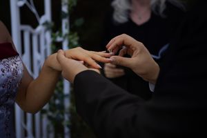 Two hands hold a small delicate origami paper crane against a dark background.