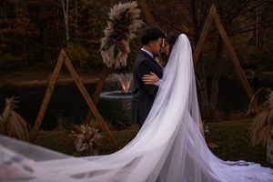 Wedding couple walking through autumn forest with embroidered veil flowing behind them.