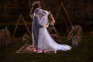 Dreamy wedding scene with flowing white dress and rose petals scattered on grass at golden hour.