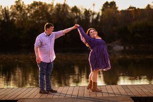 A couple dances together on a wooden dock at sunset by a serene lake.