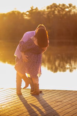 A person bending down on a wooden dock during golden sunset hour, creating a silhouette against the glowing water.