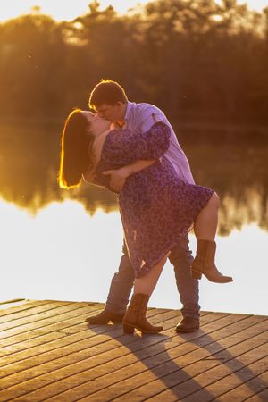 A couple on a wooden dock at sunset, silhouetted against golden light reflecting on calm water.