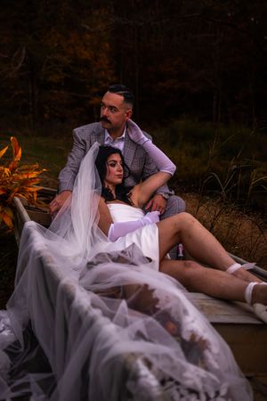 Romantic couple lounges together on white fabric in moody forest setting during intimate outdoor photo session.