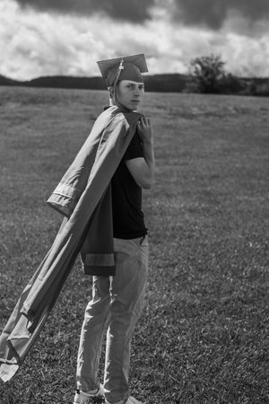 A black and white sequence of a person carrying and tilting a large cardboard rocket in a grassy field.
