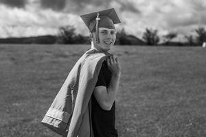 Black and white photo of a person in graduation cap and gown celebrating outdoors.
