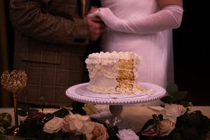White wedding cake with delicate floral decorations displayed on a stand against a dark background.