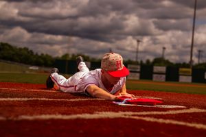 Baseball player slides into home plate during a dramatic play on a dirt infield under cloudy skies.