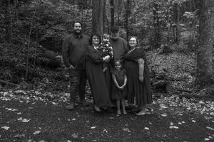 A vintage black and white photograph shows a group of people standing together in a wooded outdoor setting.