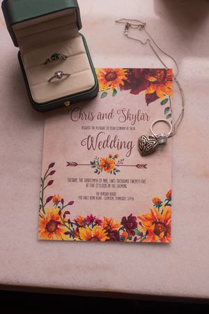 Wedding invitation cards decorated with vibrant autumn flowers and ring boxes arranged on a pink surface.