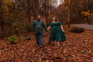 A couple walks together on a path covered in vibrant autumn leaves during a fall photoshoot session.
