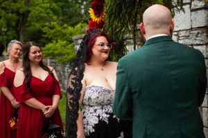 Wedding party members share joyful moments in an outdoor garden setting wearing burgundy and dark green attire.