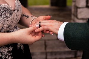Close up of hands exchanging wedding rings during an elegant outdoor marriage ceremony.