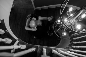 A black and white photo shows a DJ performing at a turntable setup with stage lighting in the background.