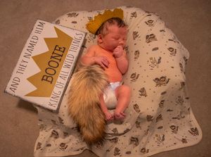 Four sequential photos show a newborn baby lying on a patterned blanket with milestone cards marking growth progress.